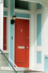 Fototapeta premium Red front door on modern doorstep in the neighborhood in downtown major city with white accent paint and blue