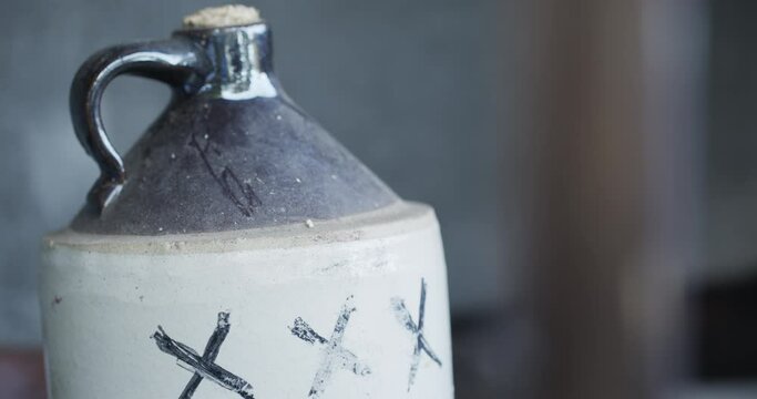 A corked ceramic jug of moonshine liquor marked with the letters 'XXX' sits with the background out of focus.