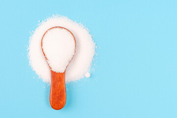 Erythritol powder in a wooden spoon close-up on blue background.