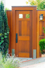 Brown wooden and modern security gate for a front or back yard with metal hardware and trees shrubs and bushes our front