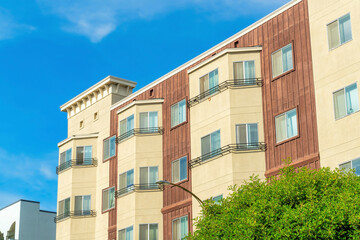 Decorative building facade with cream colored beige and brown slatted wood panneling on green tree canopy foreground