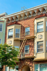 Brown and beige modern building with orange fire escape metal ladder for security and front yard tree in midday sun