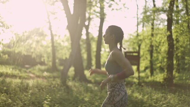 Side view of a young athletic woman running in the sunny countryside, sportsman joining her on the run. Healthy lifestyle concept. Slow motion.