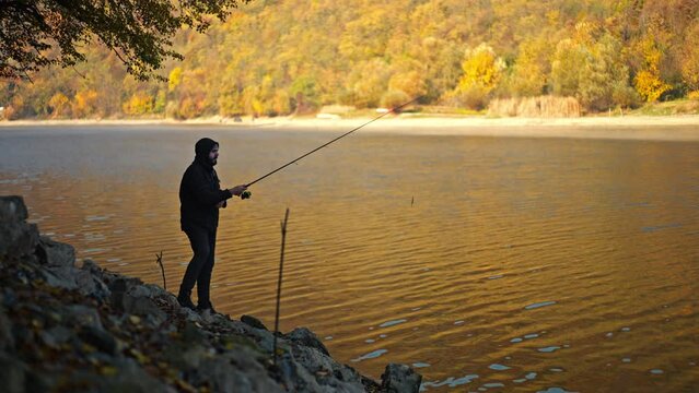 Young man in black hoodie and jacket throwing a spinning rod into the lake.