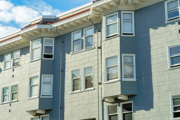 Building facade with gray and green stucco paint and a great many windows with blue and cloudy sky background