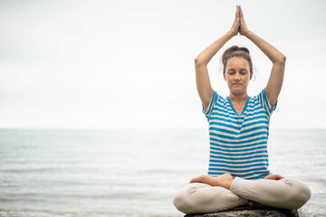 Fototapeta na wymiar Yoga woman meditation in lotus position at pebble sea beach sunset sky horizon healthy lifestyle