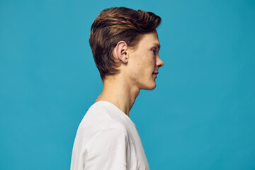 a man in a white T-shirt stands sideways to the camera on a blue background