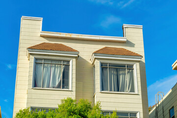 Close view of single building facade with red adobe roof tiles and cream or beige stucco paint exterior