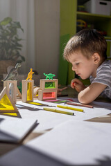 A cute little boy draws on the floor of his room. Circles on a white sheet the shadows from the dinosaurs cast from the sunlight.