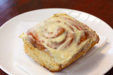 Frosting cinammon roll on white plate. Sweet dessert at bakery