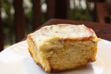 Close up on icing cinammon roll on white plate. Sweet dessert at bakery