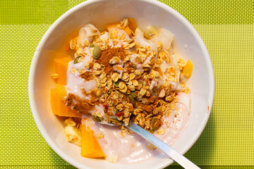 Breakfast bowl with muesli, tropical fruits, cinnamon and yogurt over green tablecloth. Healthy dieting concept - Powered by Adobe