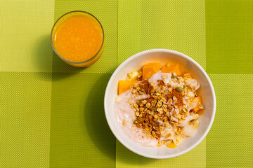 Granola, fruits, yoghurt bowl and orange juice over green background. Healthy breakfast concept