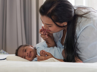 Pretty new mom looking at newborn baby boy with love and happiness while son lying down side way on the bed. Multiracial family, diverse and unconditional love.