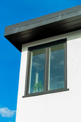 Modern metal framed glass window with black accent paint on white stucco exterior of house or home with dark flat roof