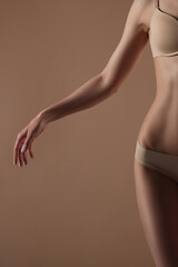 Thin young woman in underwear on beige background