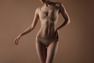 Thin young woman in underwear on beige background - obrazy, fototapety, plakaty