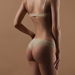Thin young woman in underwear on beige background