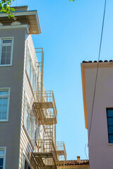 Gap between buildings in the city with metal fire escape ladder in sun and stucco buildings with blue sky background