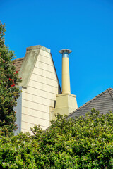 Hidden metal chimney vents with white wooden facade and brown roof with front yard trees and blue sky background