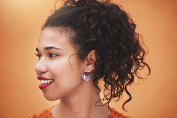 Face of happy young hispanic woman thinking of ideas, beauty and gen z fashion against an orange color studio background. Smile, youth and happiness of confident girl with curly hair, vision and joy