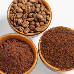 Cups with roasted coffee beans and ground coffee, white background and copy space.