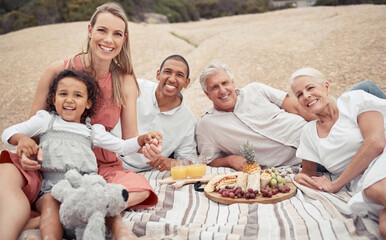 Portrait, love and happy interracial family having a picnic on the beach and smile while having...