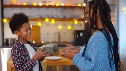 Side view of happy African-American woman giving christmas present to preteen son