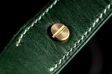 Part of a leather product or belt in green on a black background.