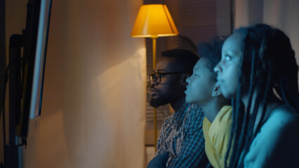 Side view of African-American family sitting near tv screen watching movie in living room