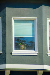 Lone window on house overlooking the front yard with white accent paint and gray stucco exterior in a neighborhood