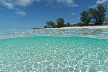 Split Shot of deserted island in the bahamas. Clear blue aqua water with sun rays shining through to white sandy bottom. 