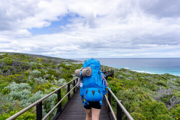 Hiker wearing large backpack full of gear walking along wooden footpath on the Cape to Cape track...