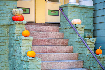 Red cement stairs with green stone brick wall and black metal hand rail with yellow front door with pumpkin decorations on porch