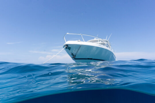 Luxury Boat Sitting On Anchor, Floating In Deep Blue Water With Blue Sunny Skies In Background. Split Shot Of Anchor Line And Bow Of Luxury Fishing Boat As It Floats In The Ocean.