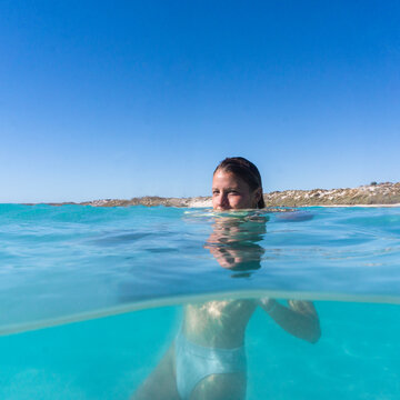 Square split shot of woman in the ocean half above water half below water surface. Woman is wearing bikini and water is clear aqua blue. Taken in Coral Bay, Western Australia. 