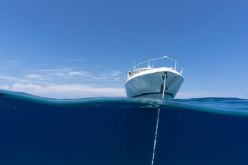 luxury boat sitting on anchor floating in deep blue water with blue sunny skies in background. Split shot of anchor line and bow of luxury fishing boat as it floats in the ocean. - Powered by Adobe