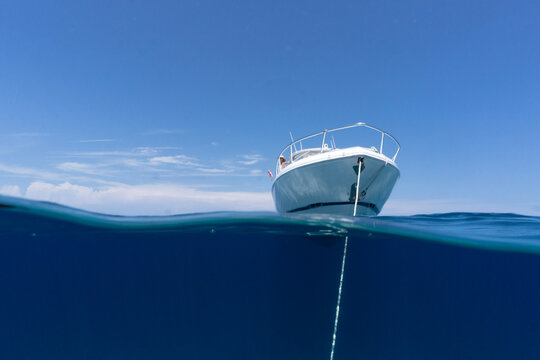 luxury boat sitting on anchor floating in deep blue water with blue sunny skies in background. Split shot of anchor line and bow of luxury fishing boat as it floats in the ocean in the Bahamas. 