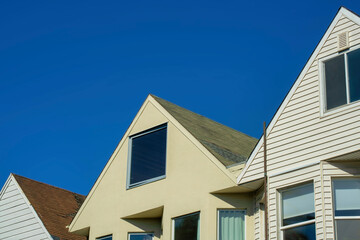 Obraz premium Row of gable house facades with wooden or timber exteriors and windows with clear blue sky background in late afternoon sun