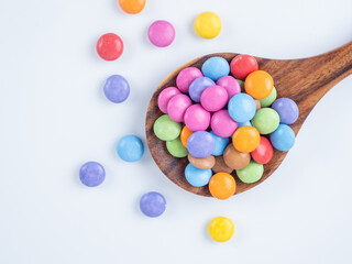 Bright multi coloured sugar coated chocolate candy presented on a teak spoon white background
