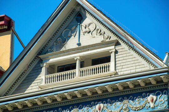 Decorative hidden balcony with victorial style and fancy facade on exterior with gable roof and blue sky background in the neighborhood