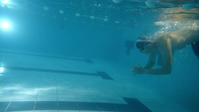 Underwater shot of a young male swimmer diving in the pool doing breaststroke tecnhique. Healthy lifestyle concept. Slow motion. 