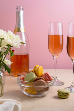 Macaroons colorful cookies in glass bowl served with champagne drink. Macarons french sweet dessert, pink background.