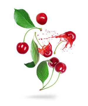 Whole and sliced cherries with juice splashes in the air isolated on a white background