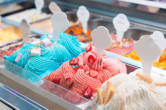 Summer sweet in italian gelateria. Close up of colourful delicious ice cream in trays in showcase fridge at confectionery shop. Price tag with mock up