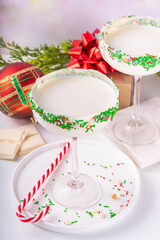 White sugar cookie martini with festive sprinkles rim. Christmas New Year alcohol cocktail with colorful red green sugar sprinkles, on Christmas decorated background with bokeh effect