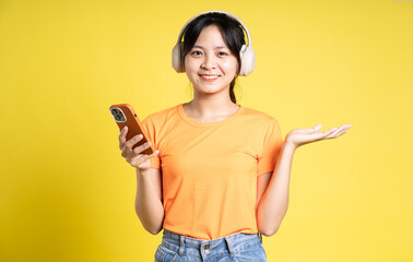 image of asian girl holding phone and isolated on yellow background