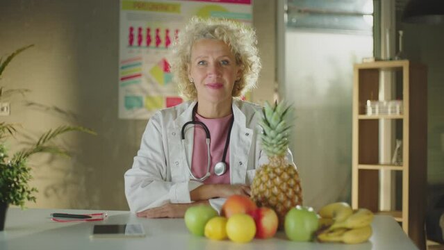 A female nutritionist sitting with different types of fruits on the desk whiling looking and smiling at camera