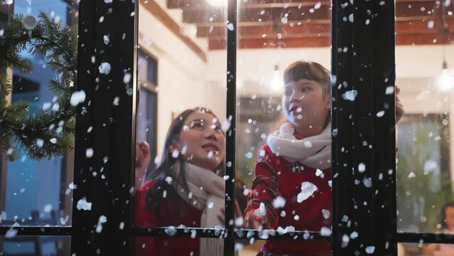 Adorable child looking at the window and first snow flakes with mother.