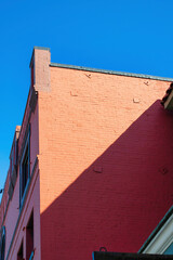 Red brick building facade on sunny surface of structure with shade streak in blue sky background in urban part of the city